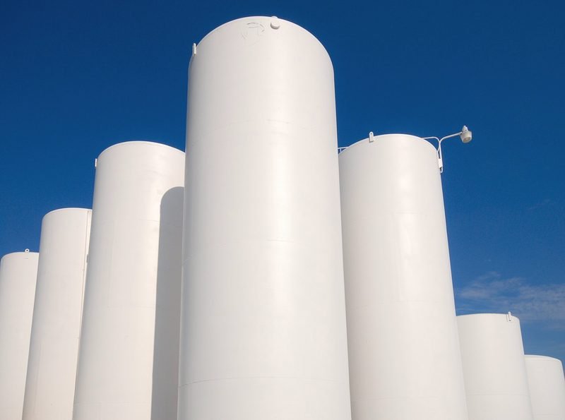 Tall white bulk propane storage tanks against a deep blue sky